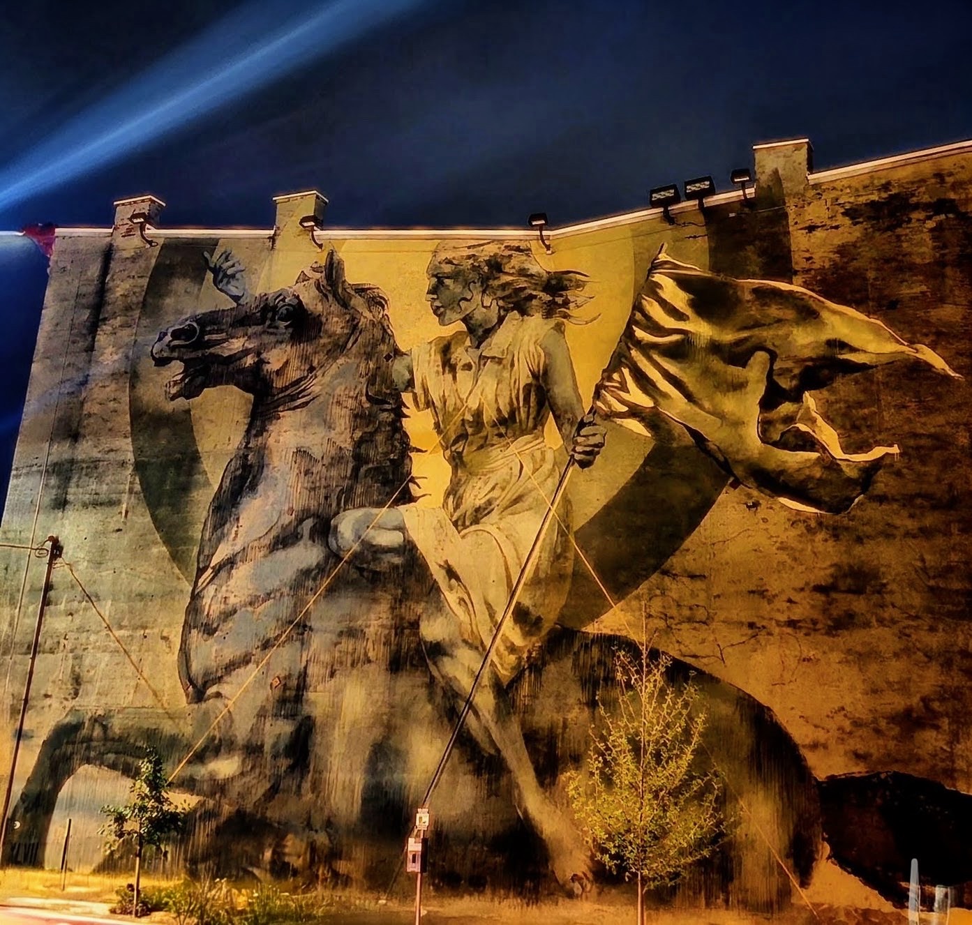 Enormous mural of a rider on horseback lit gold against a night sky