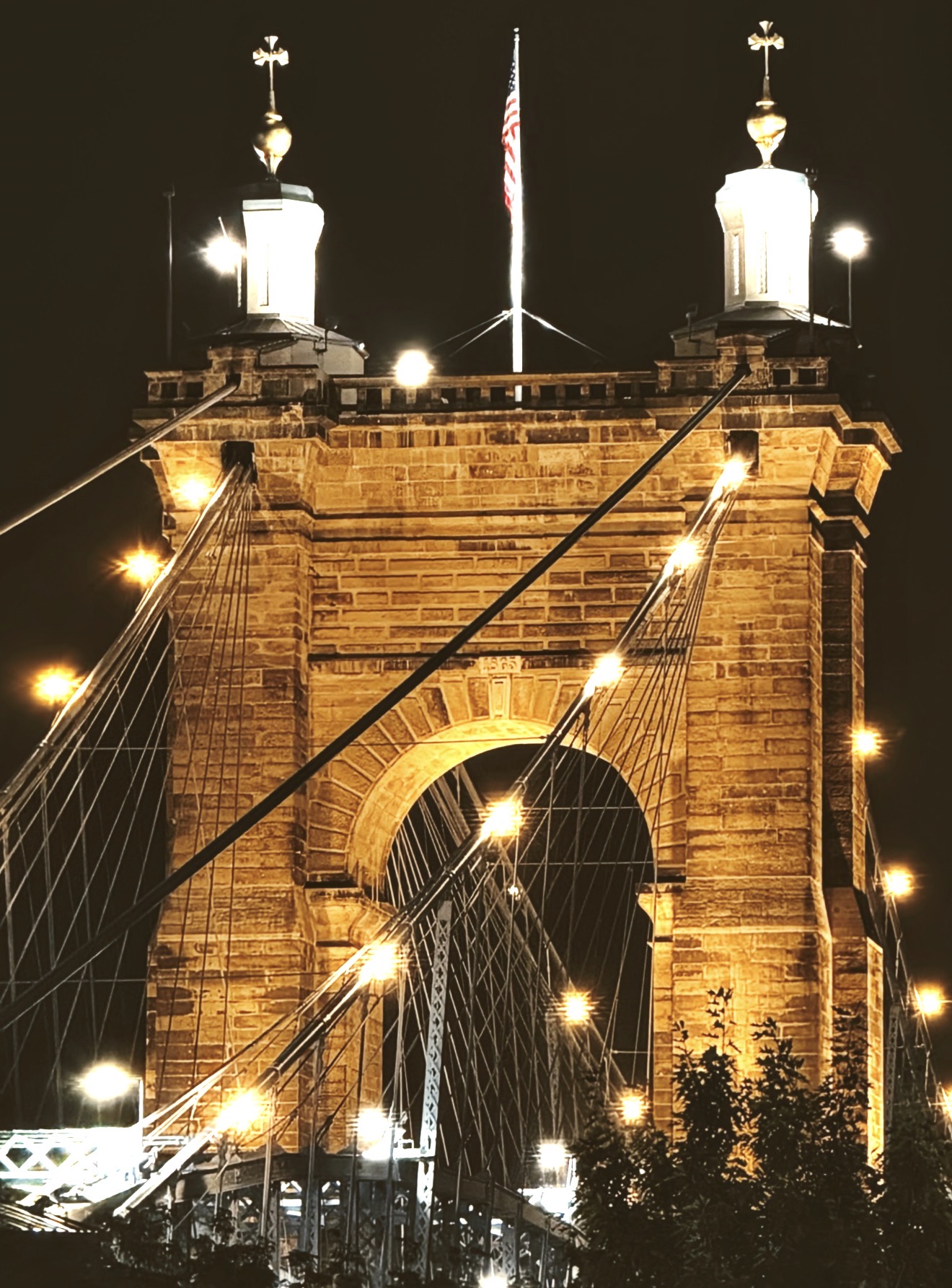 Golden lit stone tower and cables of the Roebling Bridge at night