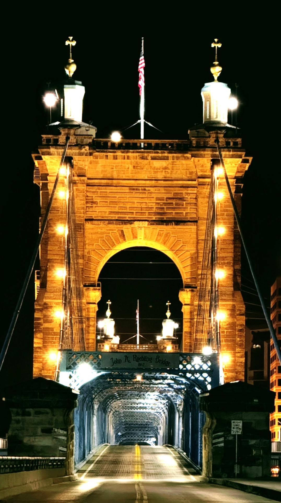 Lit stone tower of the Roebling Bridge over the empty deck at night