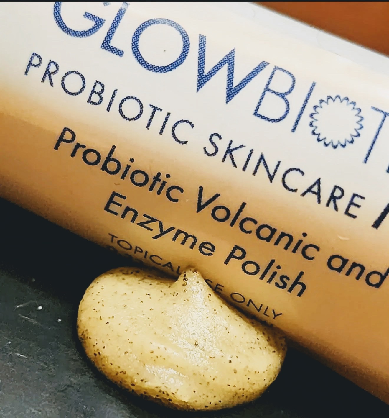 Glowbiotics probiotic volcanic enzyme polish tube beside a swatch of scrub