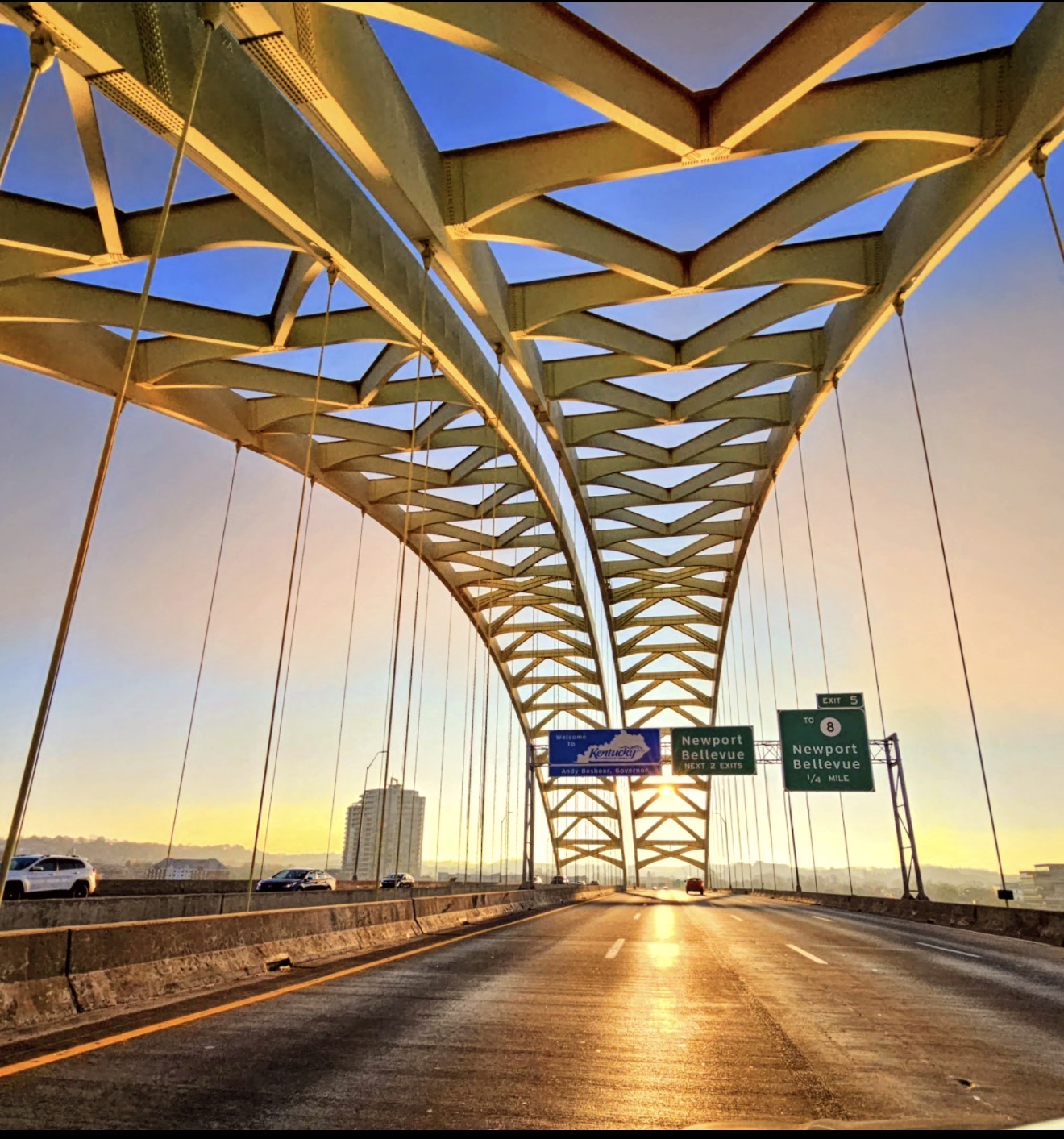 Bridge arch trusses framing a golden sunrise over the highway