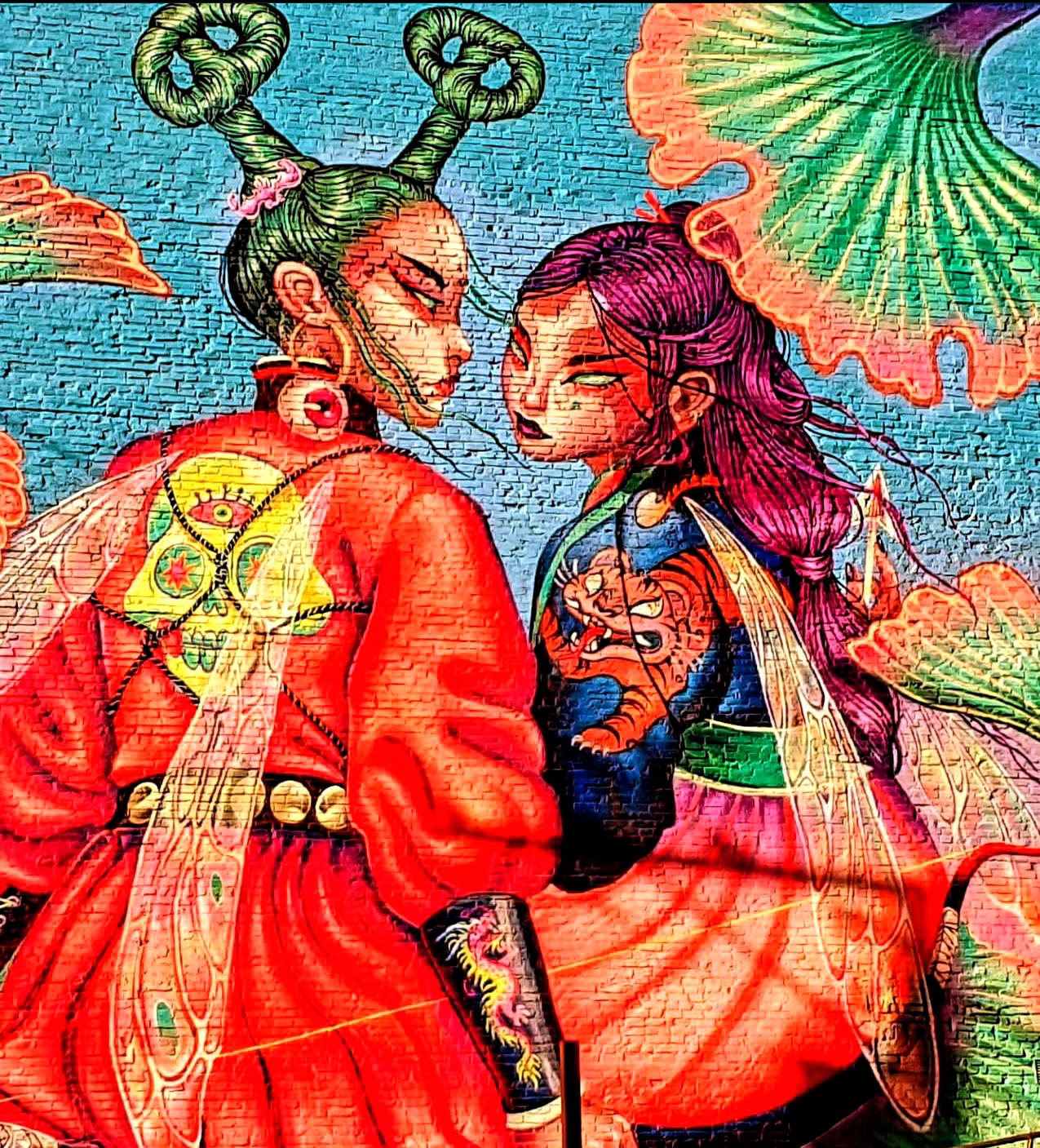 Vivid mural of two figures with green and magenta hair against a blue brick wall