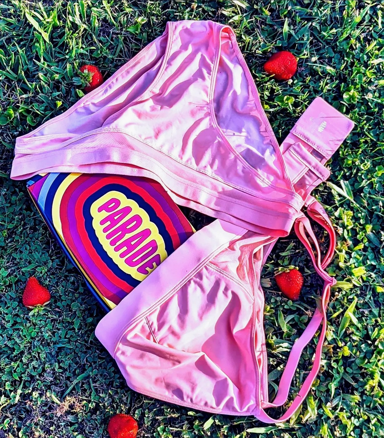 Pink Parade underwear set on grass with fresh strawberries scattered around