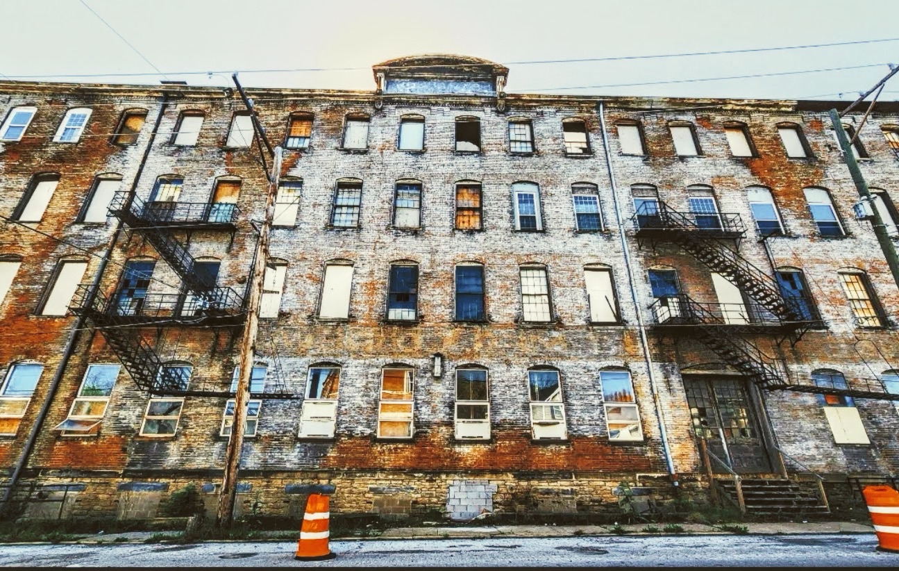 Derelict five-storey brick factory with boarded windows and iron fire escapes at dusk