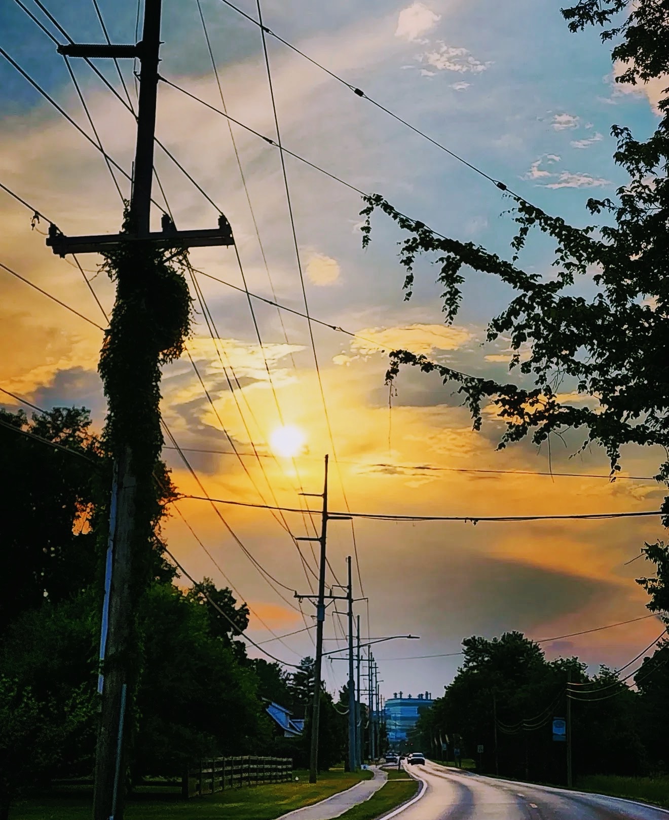 Power lines and poles silhouetted against a gold and blue sunset road