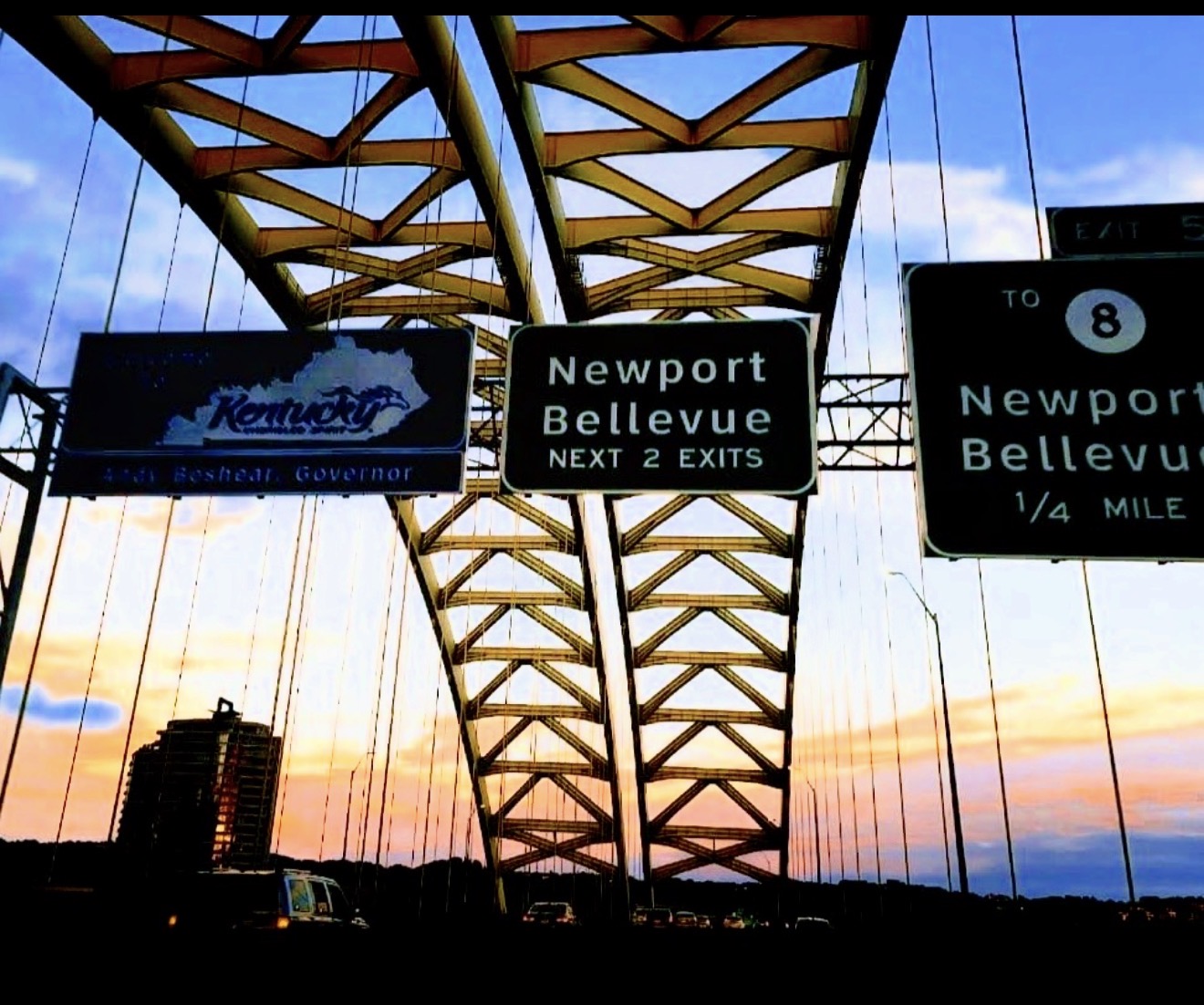 Newport and Bellevue exit signs under bridge trusses at dusk