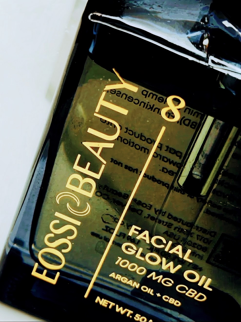 Eossi Beauty facial glow oil bottle in gold type on black, shot at a steep angle