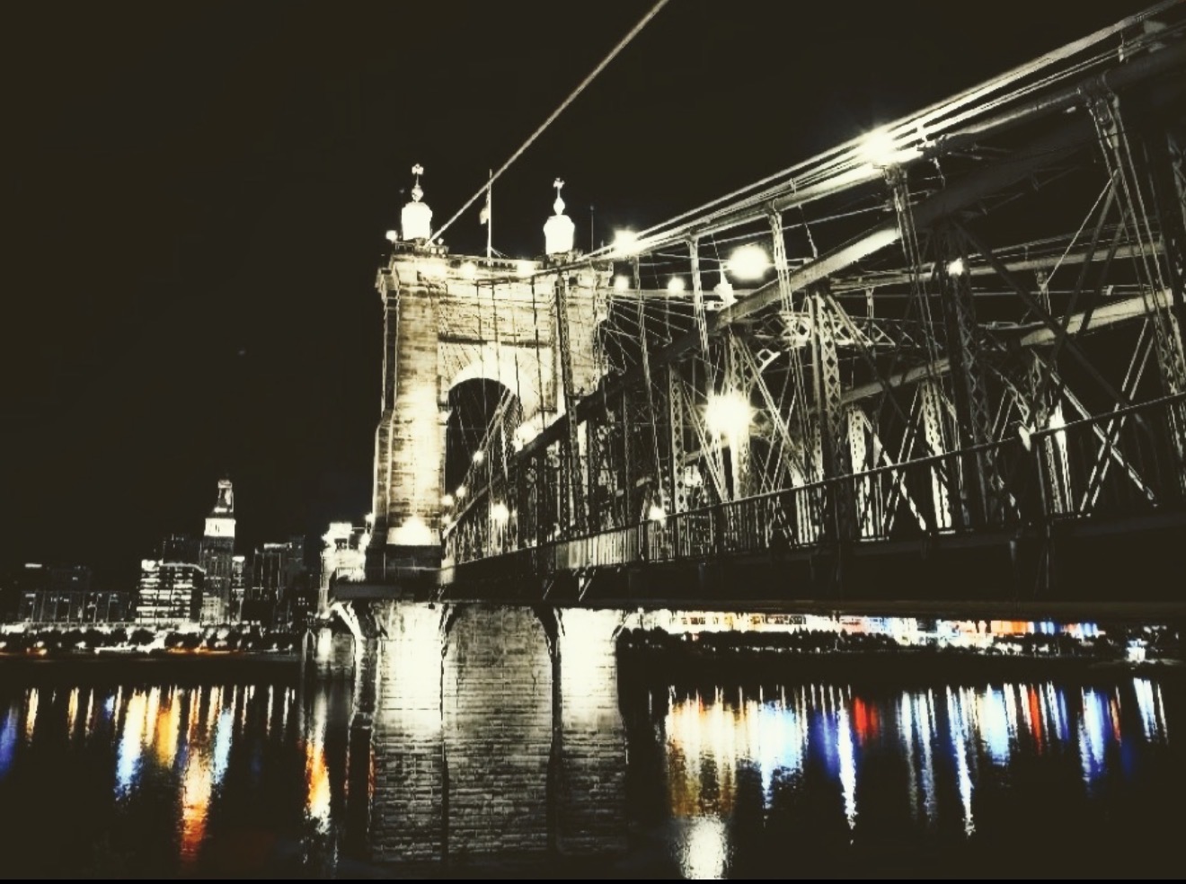 Suspension bridge lit up at night reflected in the river