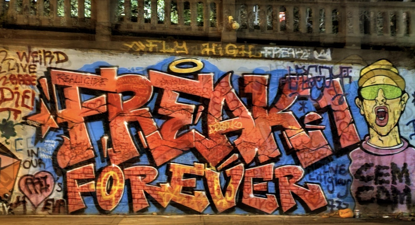 Large orange and blue Freak Forever graffiti piece under a stone bridge at night