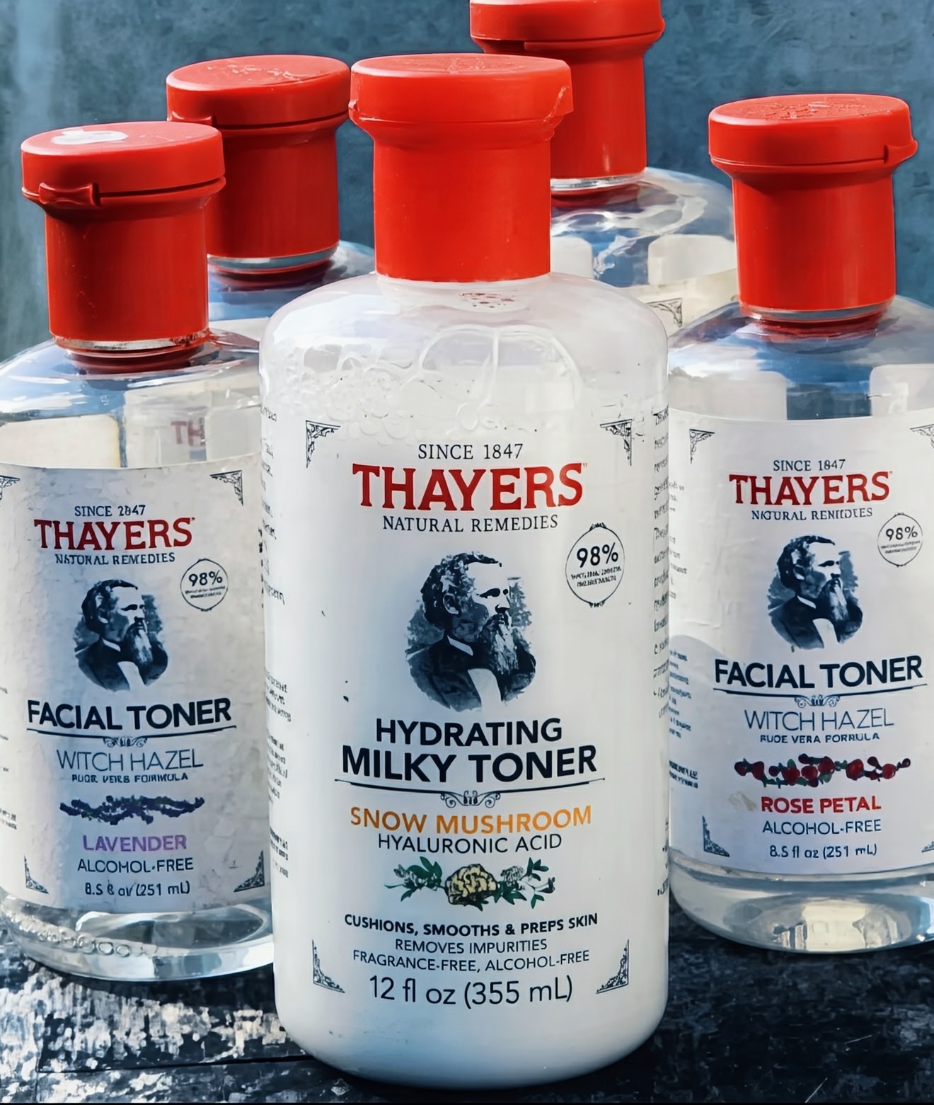 Five Thayers witch hazel facial toner bottles with red caps on weathered wood