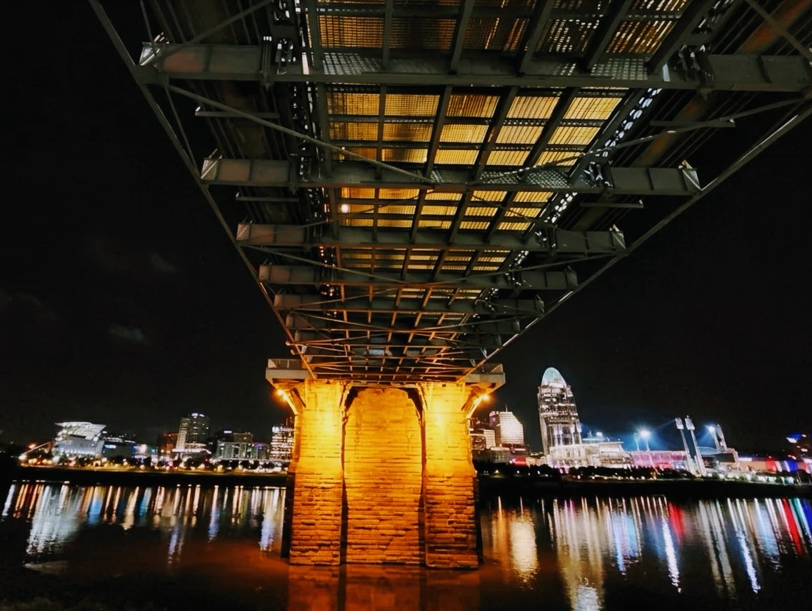 Underside of the bridge with the city skyline reflected in the river at night
