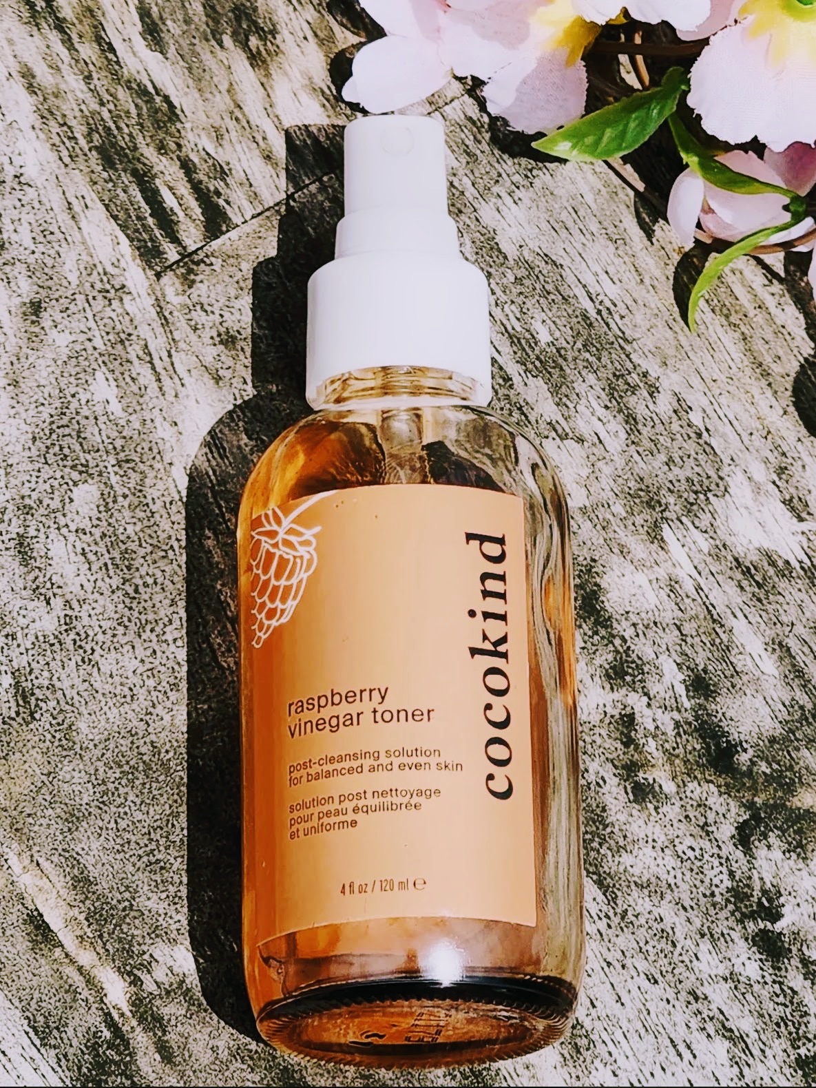 cocokind raspberry vinegar toner on weathered wood with pale blossoms