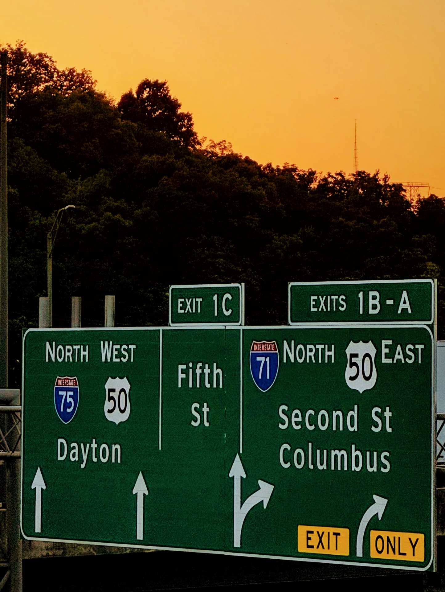 Green highway exit signs against an orange sky