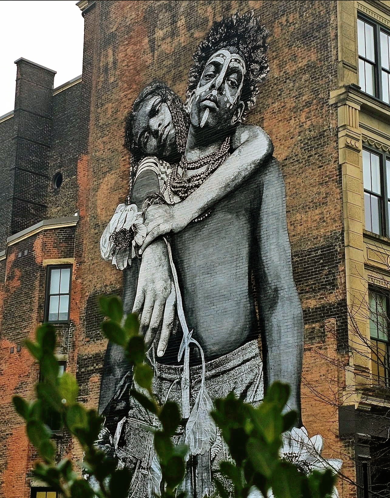 Mural of two figures holding one another on a brick wall