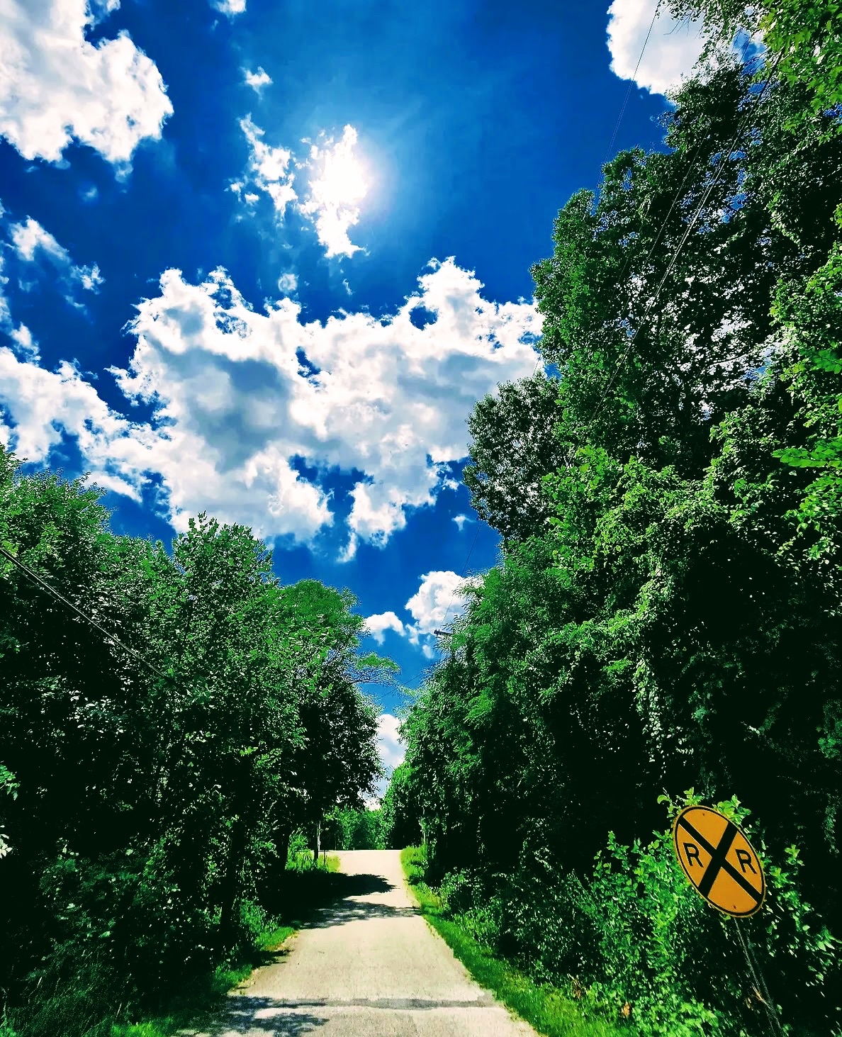 Country lane with a railroad crossing sign under blue sky and clouds