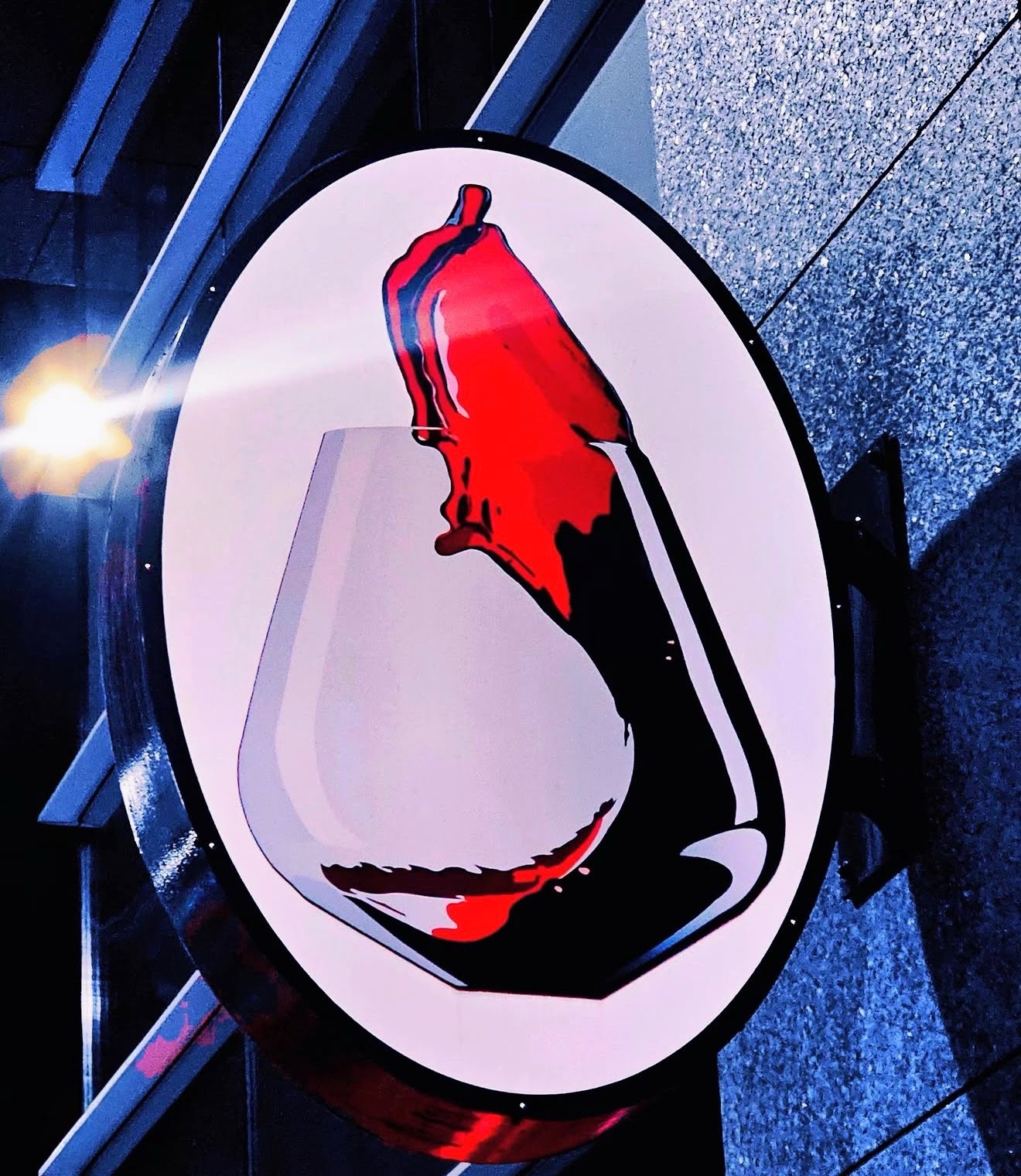 Illuminated oval sign of red wine pouring into a glass at night